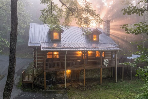 A rustic cabin with a porch, two windows, and a stone chimney.