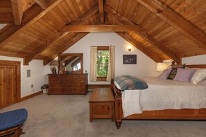 Une chambre à coucher avec un plafond en bois, un lit, une commode, un miroir et une fenêtre avec des rideaux.