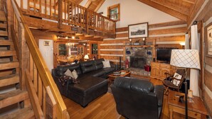 A log cabin interior with a wooden staircase, a fireplace, a black leather sofa, and a dining area. - Hounds Retreat Pet Friendly, Wood Fireplace, HotTub, WiFi, Decks (Ferguson)