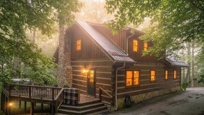 A rustic log cabin with a stone chimney, a wooden deck, and a staircase leading to the entrance. - Hounds Retreat Pet Friendly, Wood Fireplace, HotTub, WiFi, Decks (Ferguson)