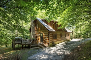 A log cabin with a porch and a stone chimney, surrounded by dense forest. - Hounds Retreat Pet Friendly, Wood Fireplace, HotTub, WiFi, Decks (Ferguson)