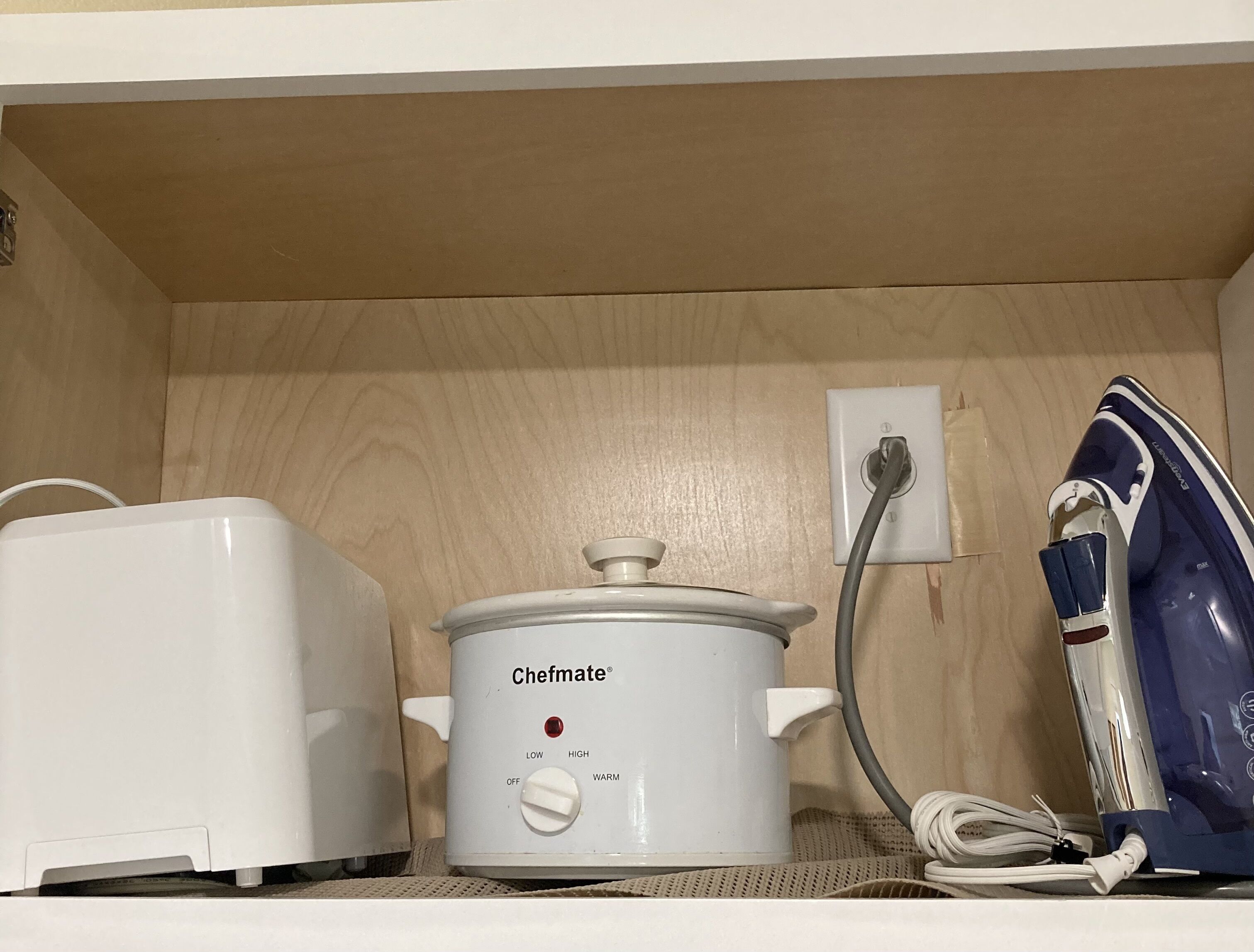 A kitchen with a white slow cooker, a toaster, and a blue iron on a wooden countertop.