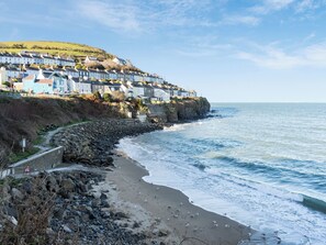 A coastal town with terraced houses along the cliffside, a rocky beach, and a clear sky.