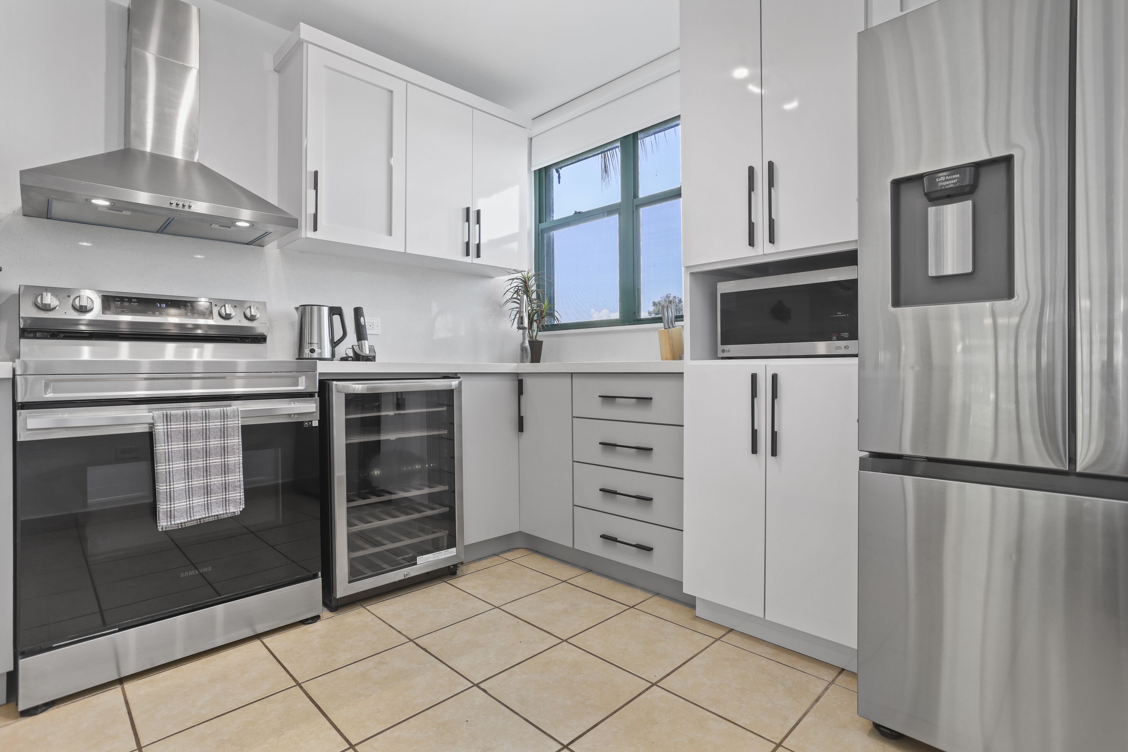 A modern kitchen with stainless steel appliances, white cabinetry, and a large window.