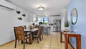 Una cocina moderna con armarios blancos, un refrigerador de acero inoxidable y un comedor con sillas y una mesa de madera.