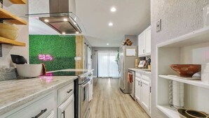 A modern kitchen with white cabinetry, a stainless steel range hood, and a green wall accent.