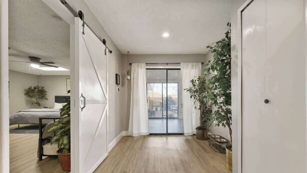A hallway with a sliding door leading to a balcony, a bed, and potted plants.