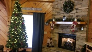 A cozy living room with a Christmas tree, fireplace, and wooden walls.