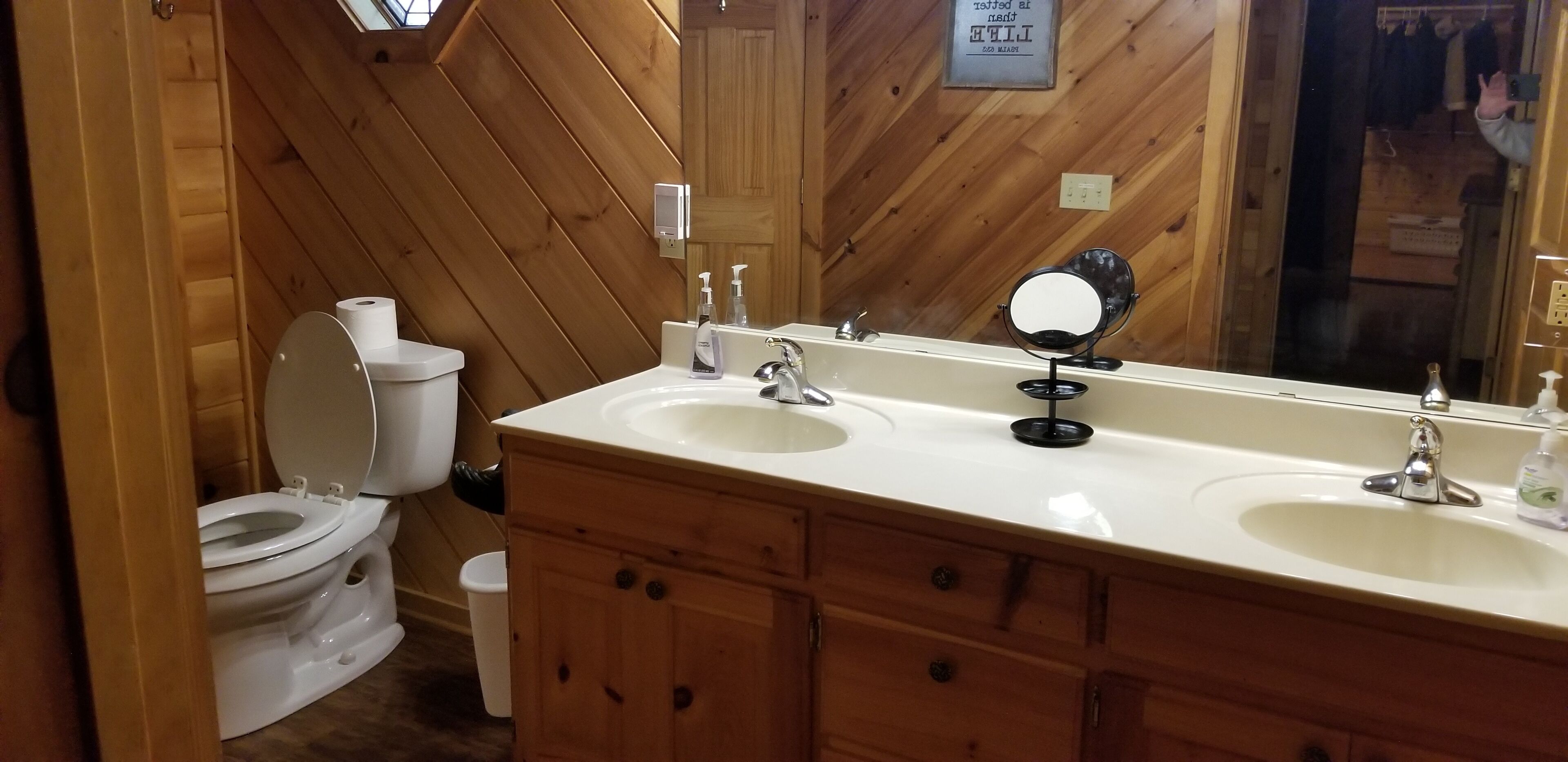 Un bagno con rivestimenti in legno, dotato di un WC, due lavabi, uno specchio e un portasciugamani.