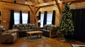 A cozy log cabin interior with a sofa set, armchairs, a coffee table, and a Christmas tree.