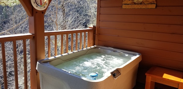 Un jacuzzi en una terraza de madera, con un termómetro y un cartel de bienvenida.