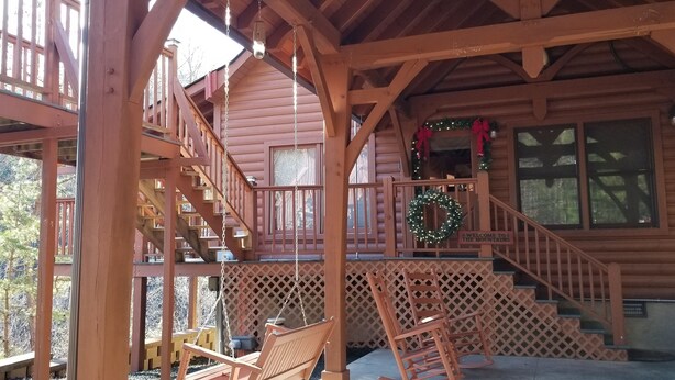 A wooden cabin with a porch, a swing, and a staircase leading to an upper level.