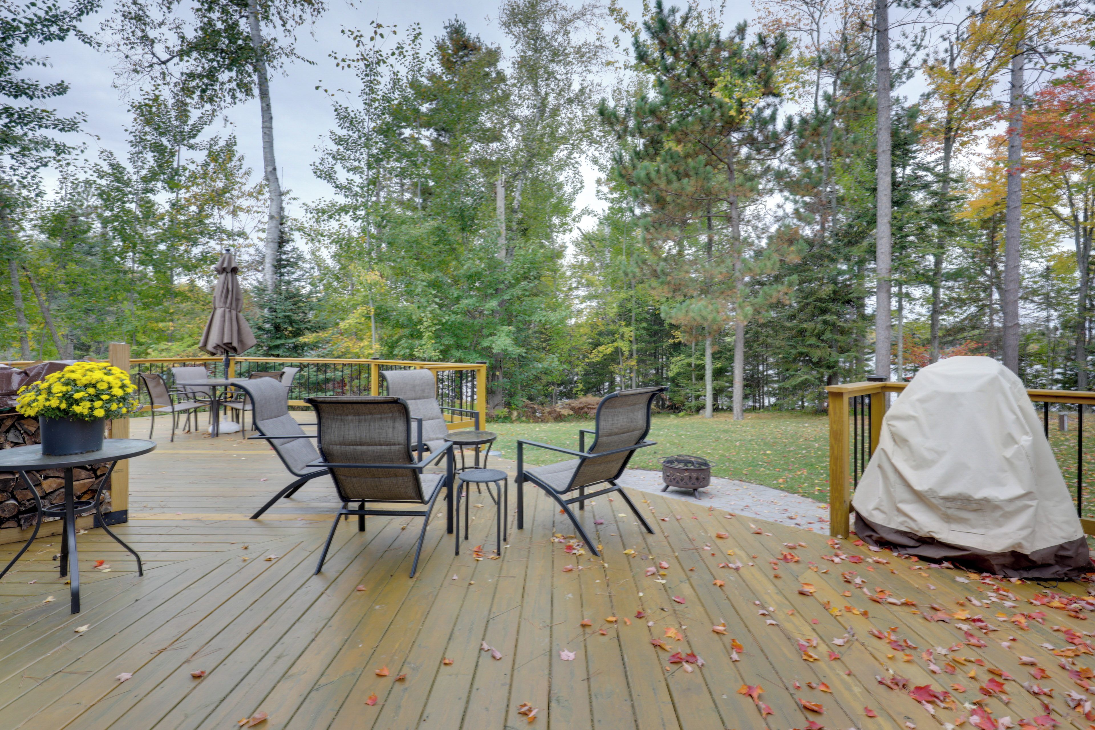 An outdoor deck with wooden flooring, metal chairs, a table with a potted plant, and a covered grill area.