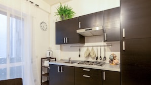 A modern kitchen with dark cabinets, a gas stove, and a stainless steel range hood. There is a clock on the wall and a plant on the counter. - [Central Station ★★  ★★★] Elegant Apartment (BARI)