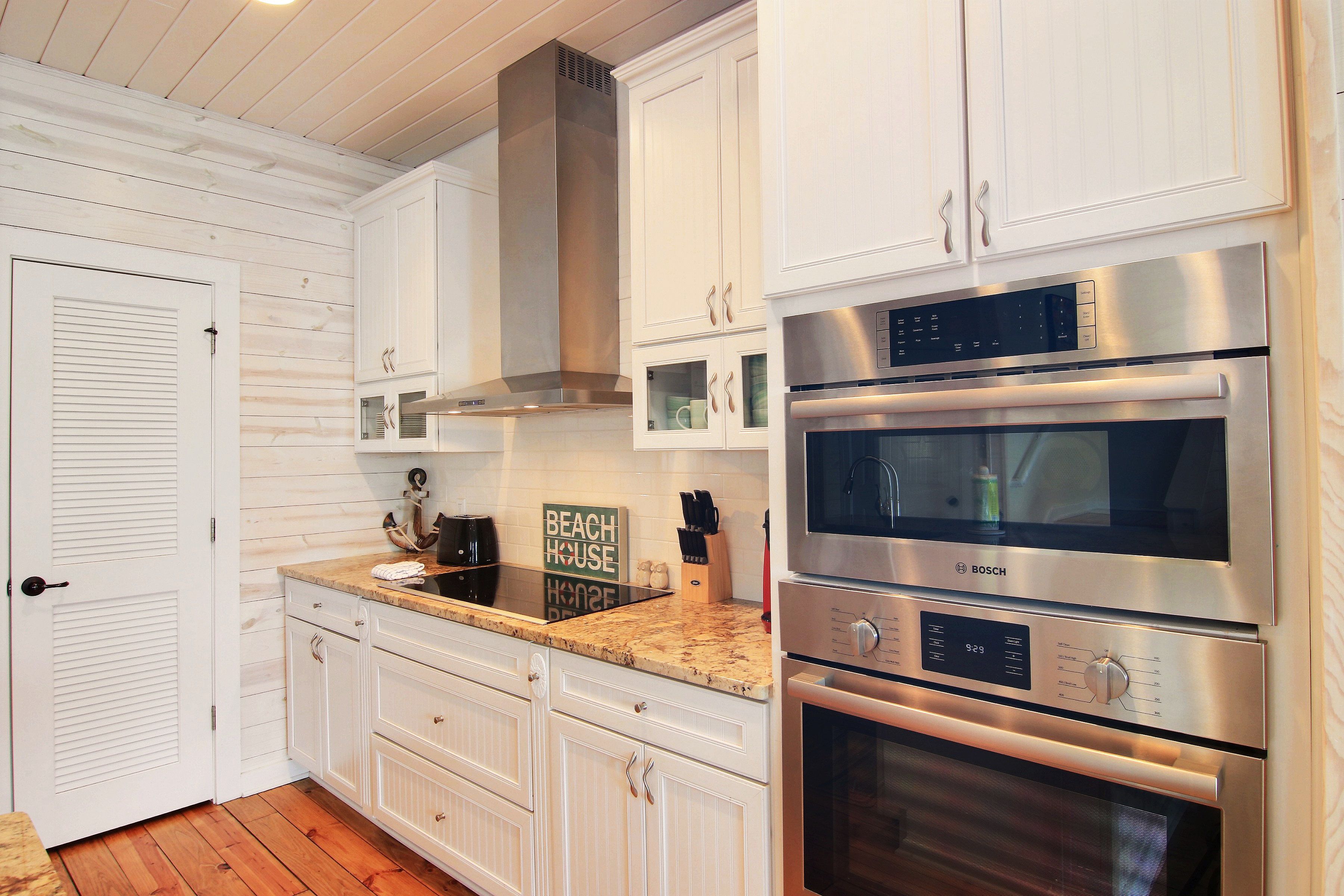 A modern kitchen with white cabinetry, stainless steel appliances, and a wooden floor.