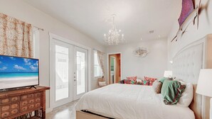 A spacious bedroom with a large bed, a television on a wooden dresser, and a chandelier. - La Dolce Vida by Silver Sands Vacation Rentals (Port Aransas)