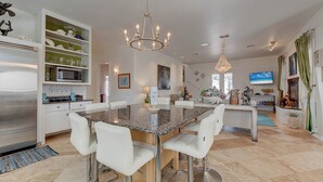 A modern kitchen with a granite countertop, white bar stools, and a stainless steel refrigerator. - La Dolce Vida by Silver Sands Vacation Rentals (Port Aransas)