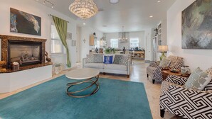 A spacious living room with a fireplace, a chandelier, and a large abstract painting. - La Dolce Vida by Silver Sands Vacation Rentals (Port Aransas)