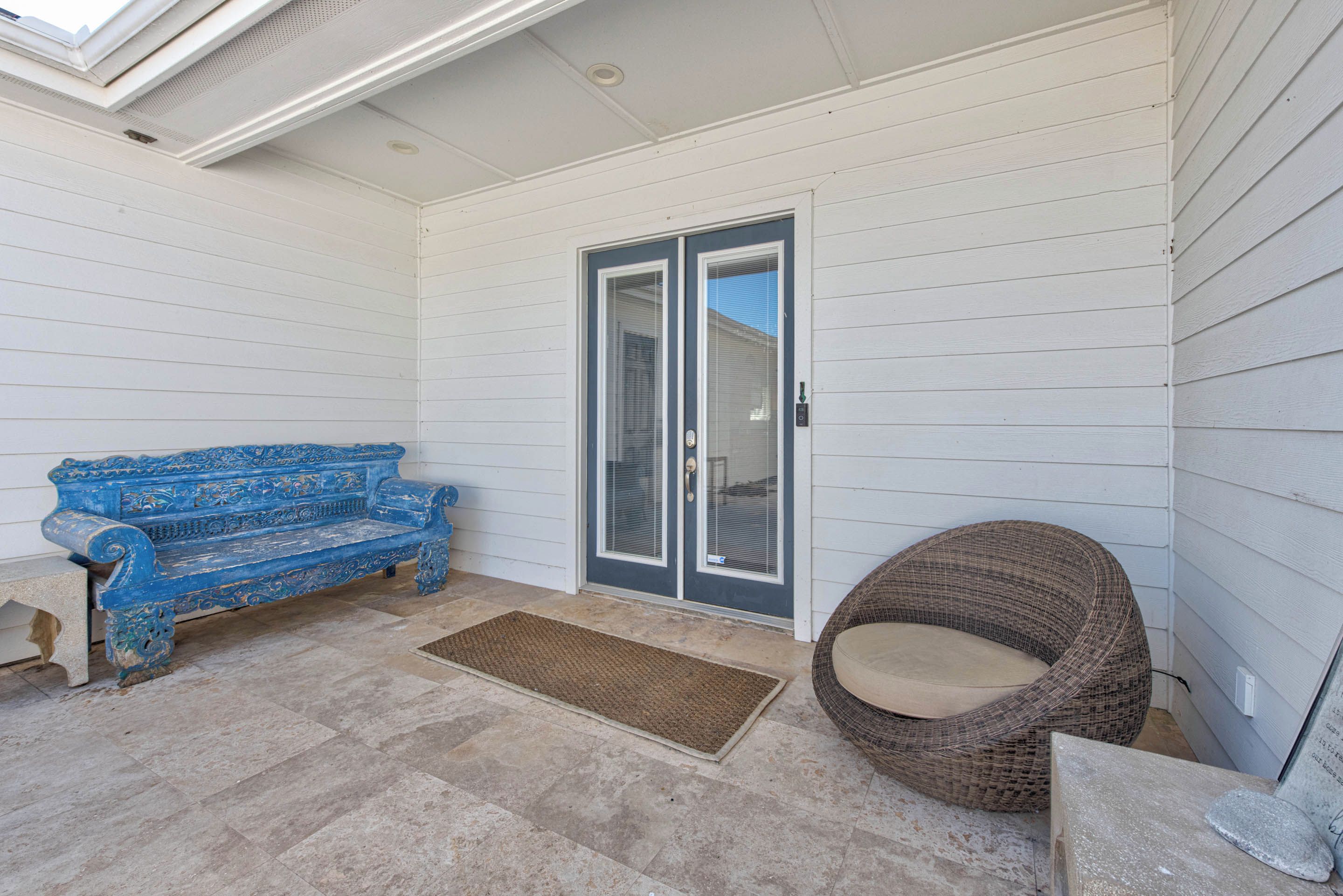 A covered porch with a blue bench, a wicker chair, and a door with glass panels.