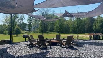 A covered outdoor seating area with chairs and a table, surrounded by pebbles and under shade structures.