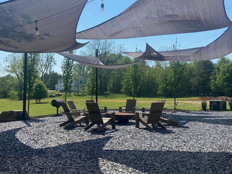 A covered outdoor seating area with chairs and a table, surrounded by pebbles and under shade structures.
