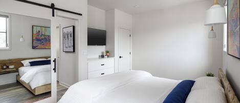 A modern bedroom with a large bed, a ceiling fan, a mounted TV, and a small plant on the dresser.