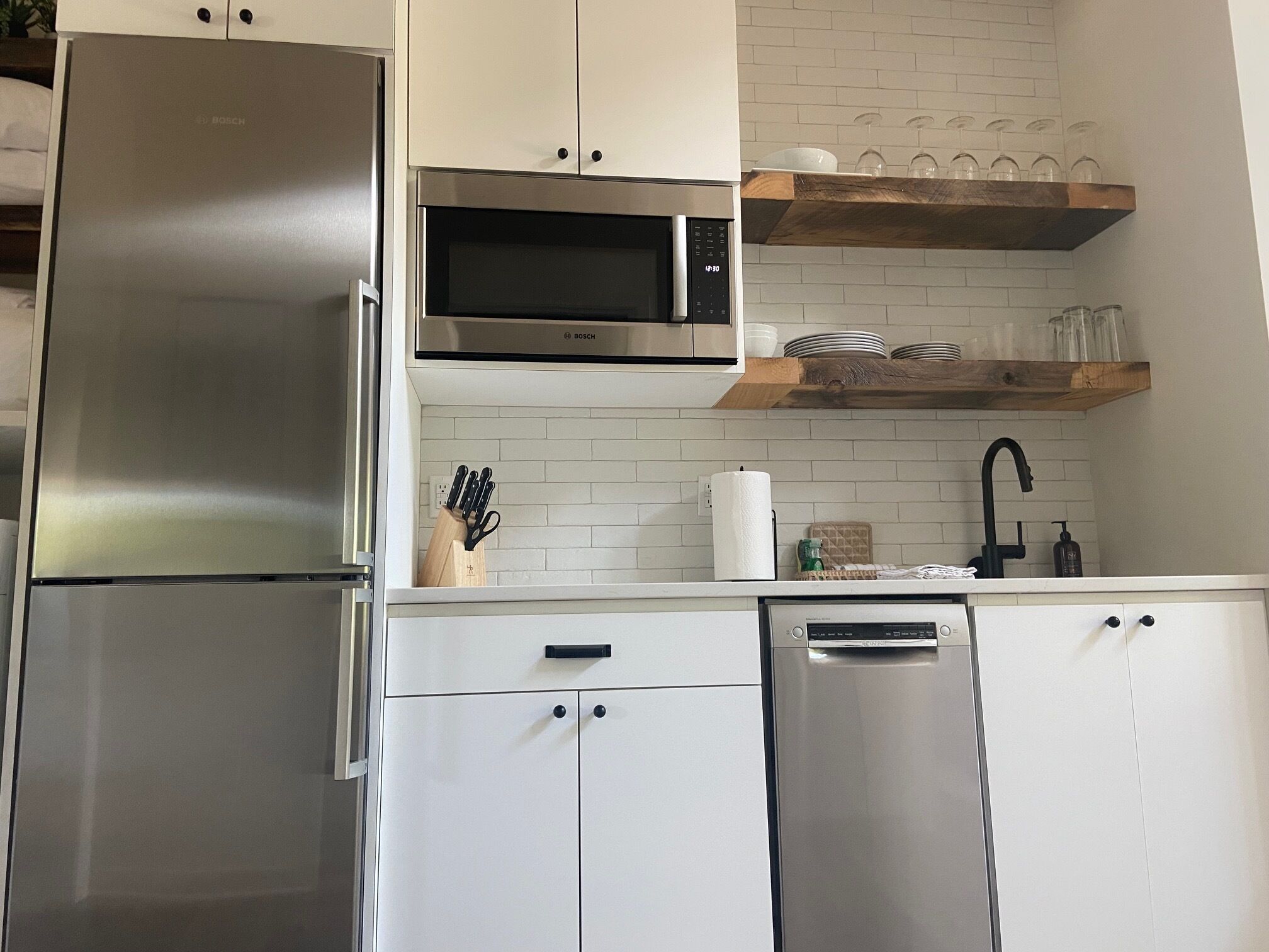 Uma cozinha moderna com eletrodomésticos de aço inoxidável, armários brancos e uma prateleira de madeira sobre a pia.