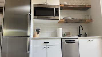 Una cocina moderna con electrodomésticos de acero inoxidable, armarios blancos y un estante de madera sobre el fregadero.