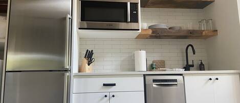 A modern kitchen with stainless steel appliances, white cabinetry, and a wooden shelf above the sink.