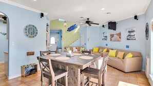A dining area with a wooden table and chairs, a sofa with yellow cushions, and a clock on the wall. - LaJuana Iguana by Silver Sands Vacation Rentals (Port Aransas)