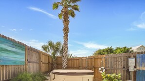 A backyard with a wooden fence, a palm tree, a hot tub, and a small garden area. - LaJuana Iguana by Silver Sands Vacation Rentals (Port Aransas)