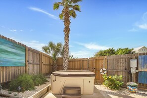 A backyard with a wooden fence, a palm tree, a hot tub, and a small garden area. - LaJuana Iguana by Silver Sands Vacation Rentals (Port Aransas)
