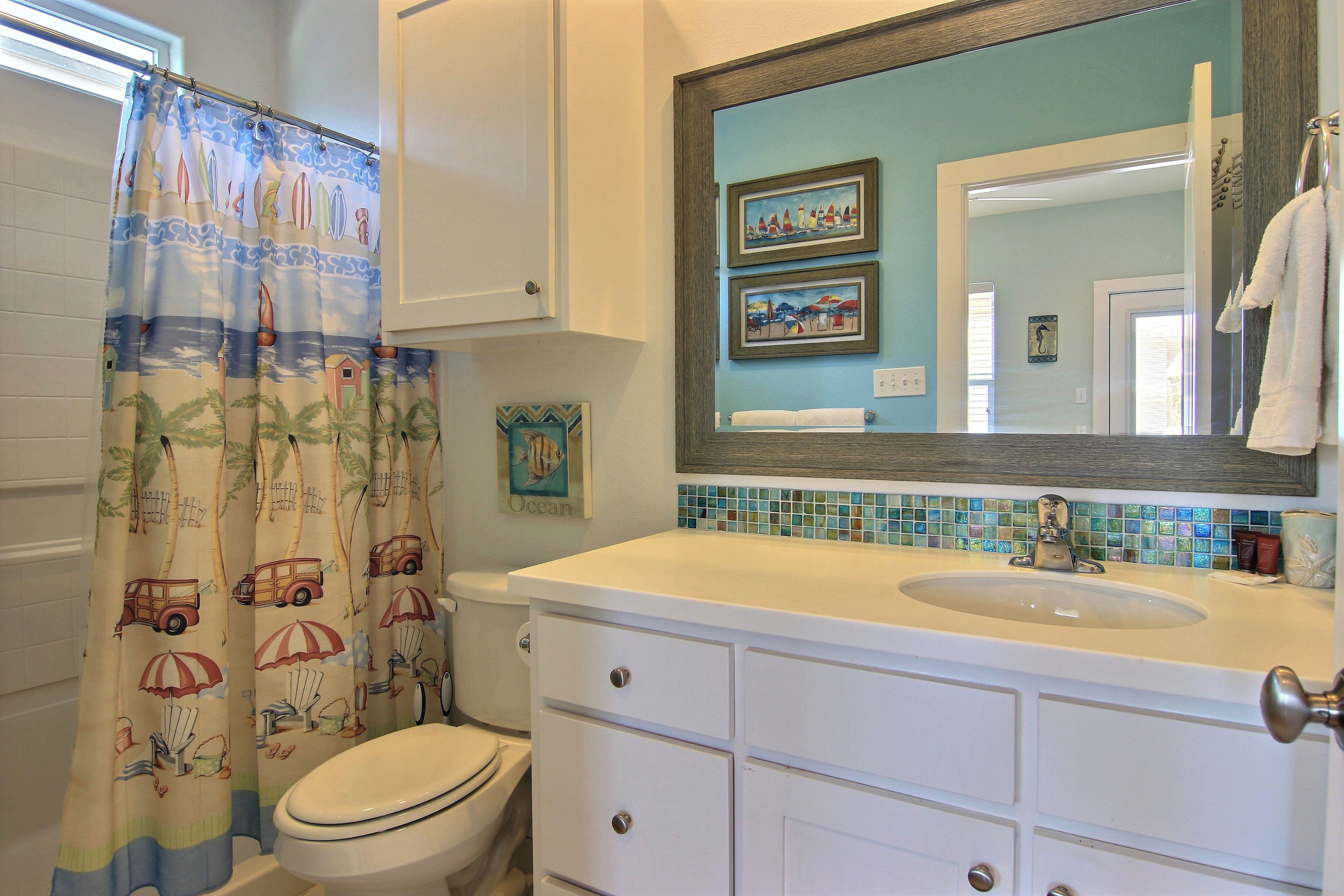A bathroom with a toilet, a sink, and a shower curtain with a beach theme.