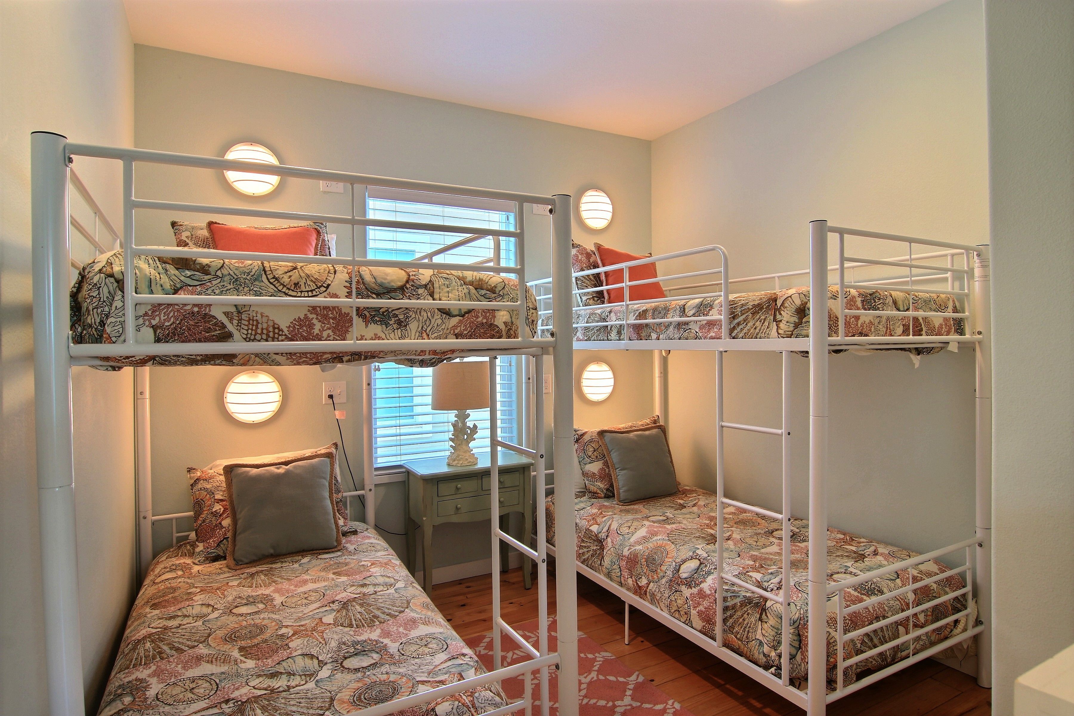 A bunk bed room with two beds, a desk, and two wall-mounted lamps.
