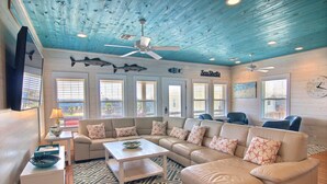 A spacious living room with a blue ceiling, a beige sectional sofa, a white coffee table, and a patterned rug. - Jumpin' Jellyfish by Silver Sands Vacation Rentals (Port Aransas)