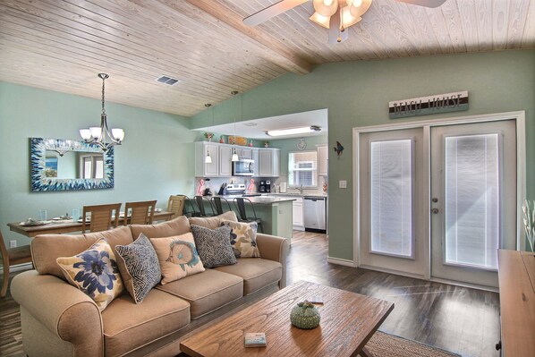 A living room with a beige sofa, wooden coffee table, and a chandelier. - Just Beachy by Silver Sands Vacation Rentals (Port Aransas)