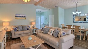 A living room with a beige sofa, a coffee table, and a dining area with wooden chairs and a table. - Just Beachy by Silver Sands Vacation Rentals (Port Aransas)