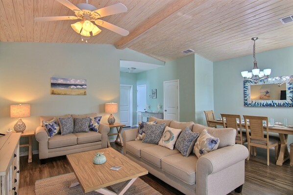 A living room with a beige sofa, a coffee table, and a dining area with wooden chairs and a table.