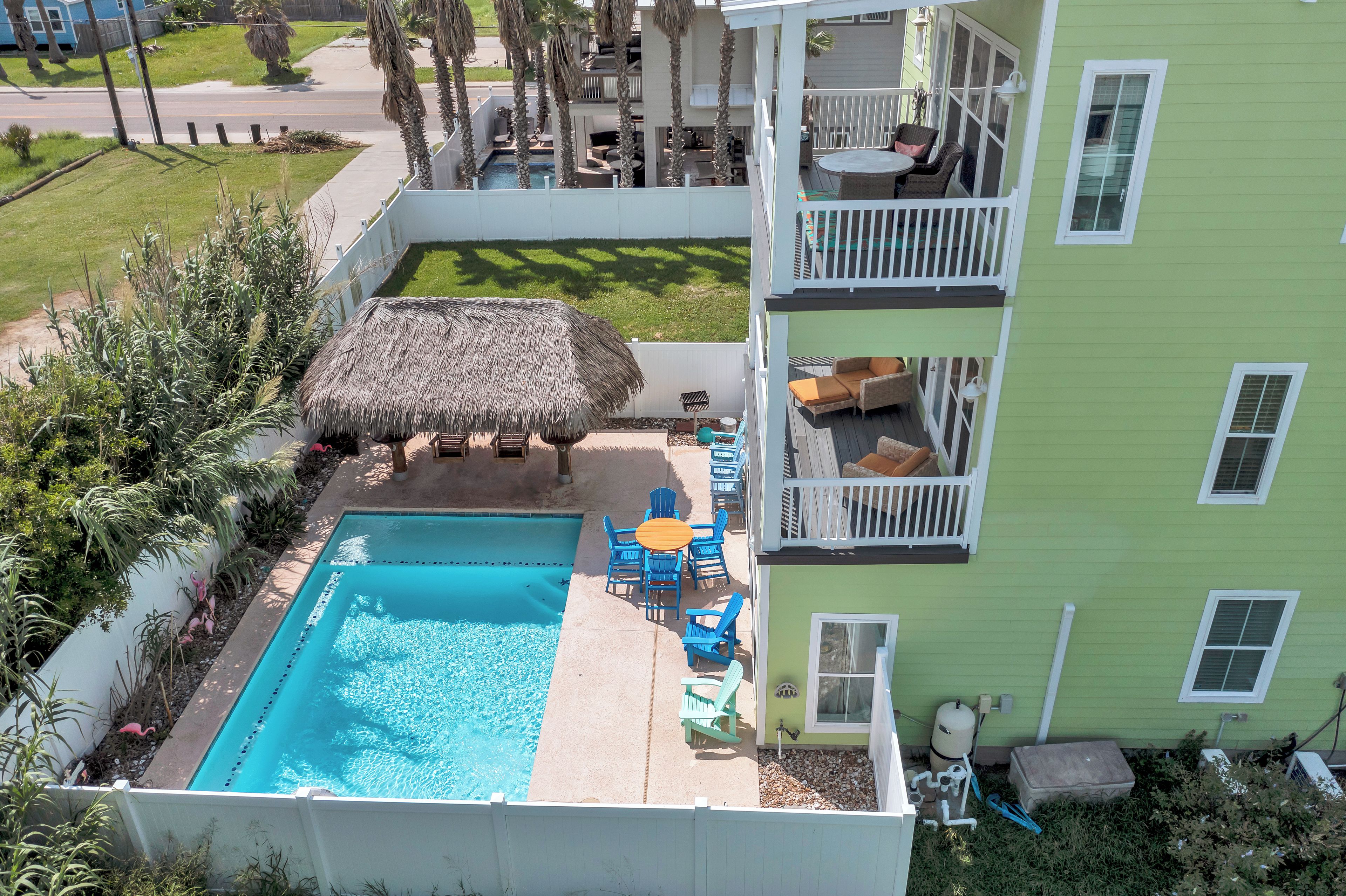 A rooftop pool area with a thatched umbrella, outdoor seating, and a view of a residential neighborhood.