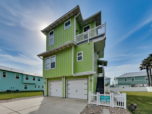 A two-story building with a green exterior, white garage doors, and a balcony on the upper floor.