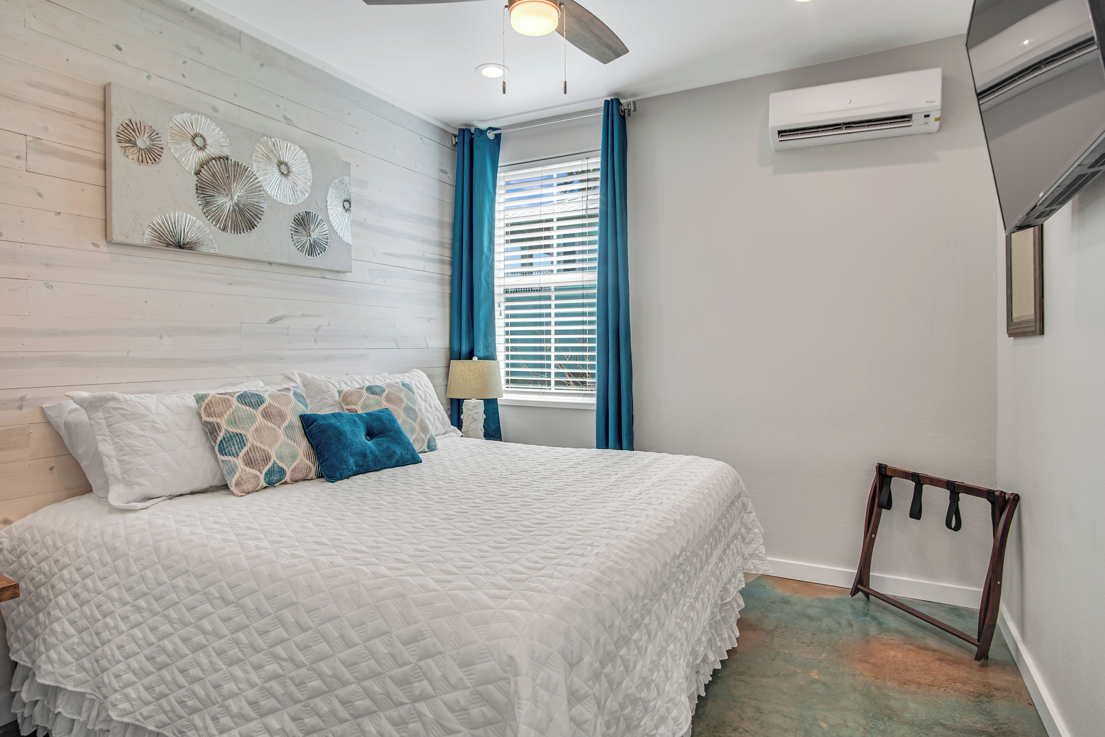 A bedroom with a bed, a ceiling fan, an air conditioning unit, and a window with curtains.