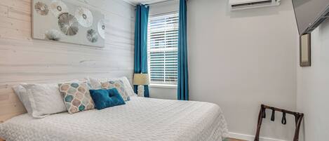 A bedroom with a bed, a ceiling fan, an air conditioning unit, and a window with curtains.