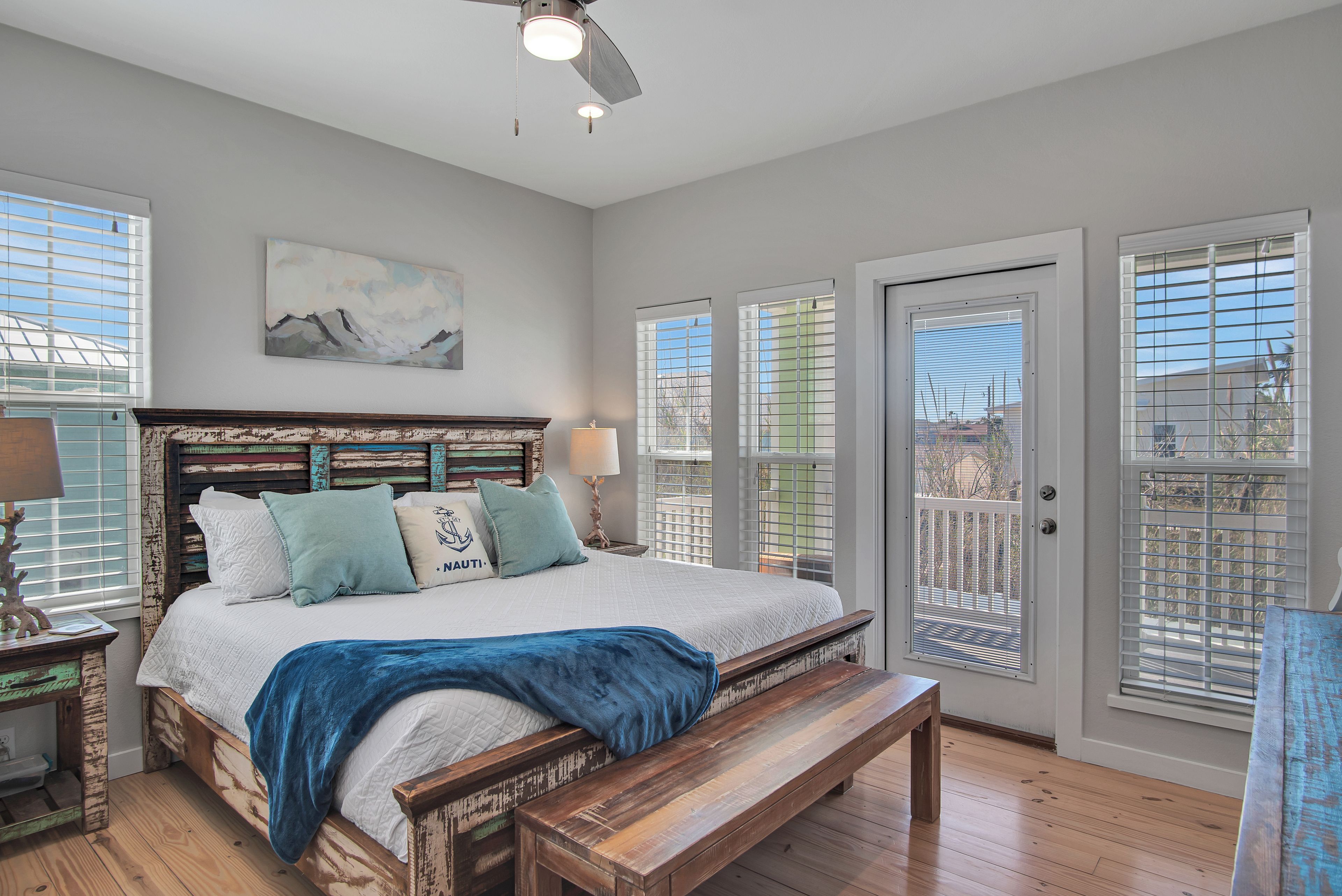 A bedroom with a bed, a bench, a ceiling fan, and a door with a view.