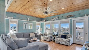 A spacious living room with a wooden ceiling, large windows, and a view of the outside. - Nauti Beach by Silver Sands Vacation Rentals (Port Aransas)