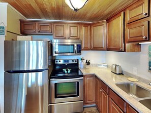 A modern kitchen with stainless steel appliances, wooden cabinets, and a granite countertop. - My Happy Place by Silver Sands Vacation Rentals (Port Aransas)