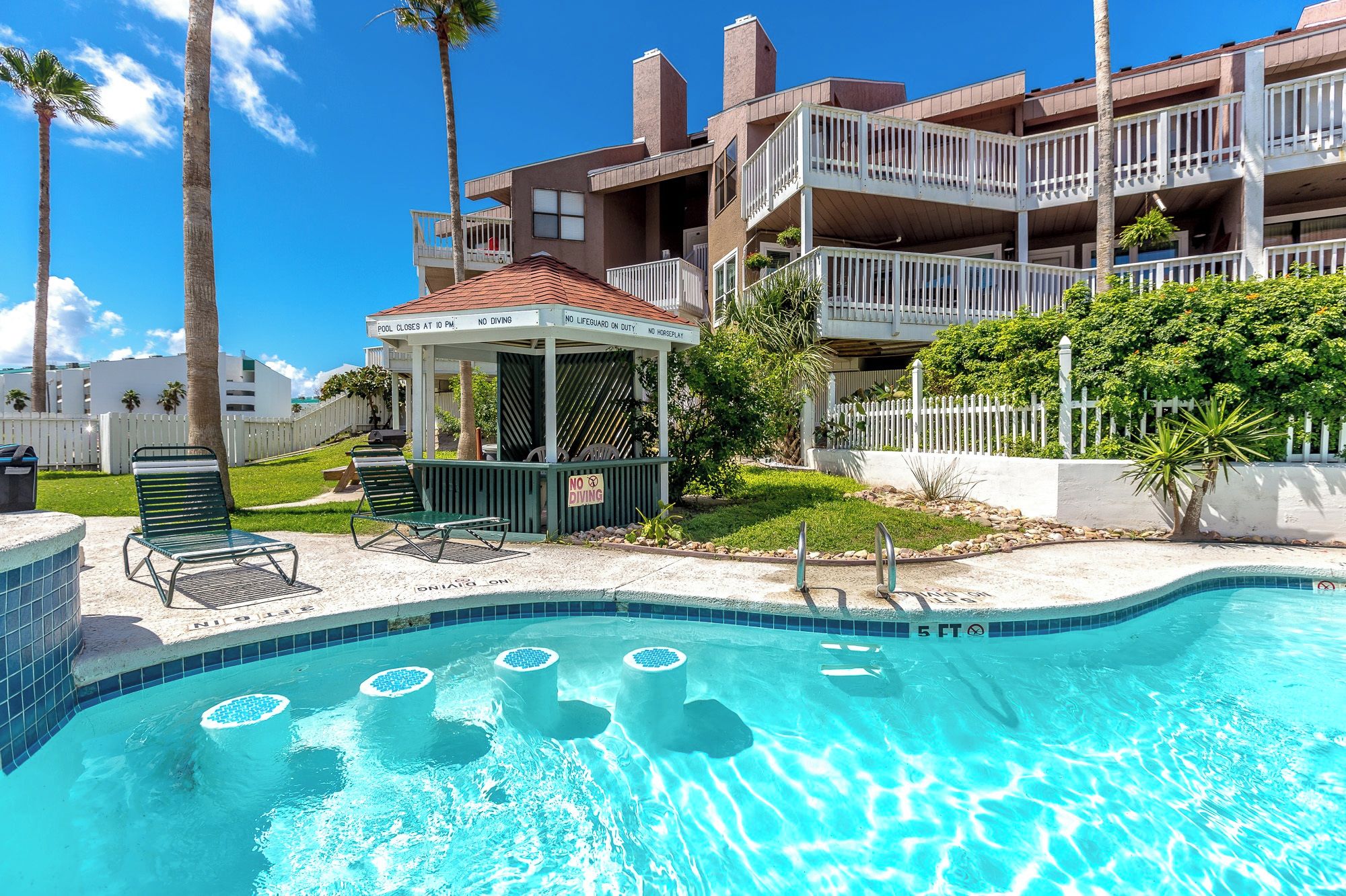 A pool area with a gazebo, lounge chairs, and a sign indicating pool rules.