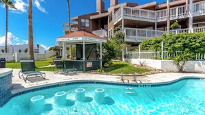 A pool area with a gazebo, lounge chairs, and a sign indicating pool rules. - My Happy Place by Silver Sands Vacation Rentals (Port Aransas)