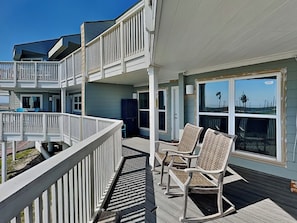 A multi-level building with a covered deck area featuring wicker chairs and a railing. - My Happy Place by Silver Sands Vacation Rentals (Port Aransas)