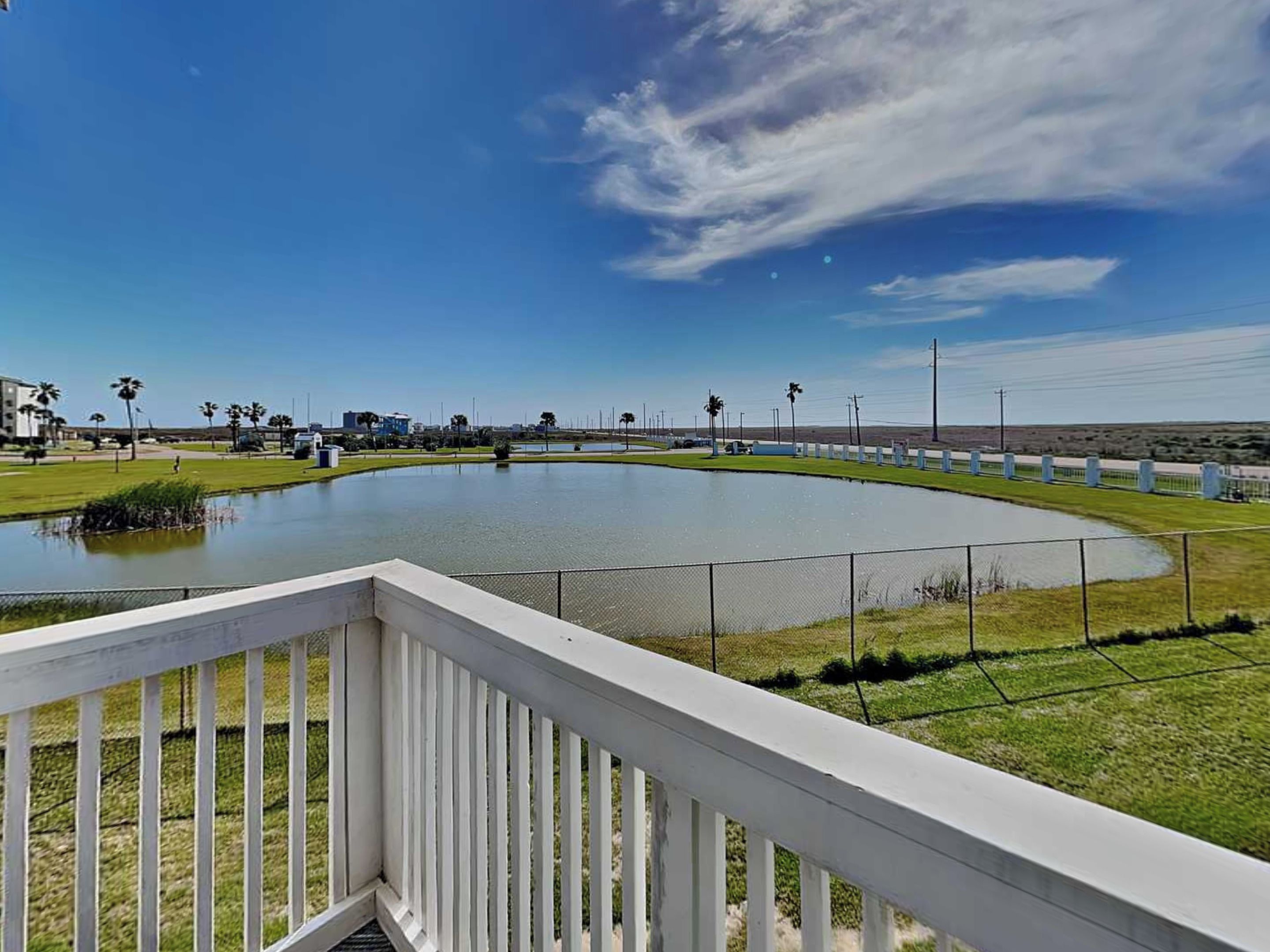A view of a water body with a white railing in the foreground, a clear sky, and distant buildings.