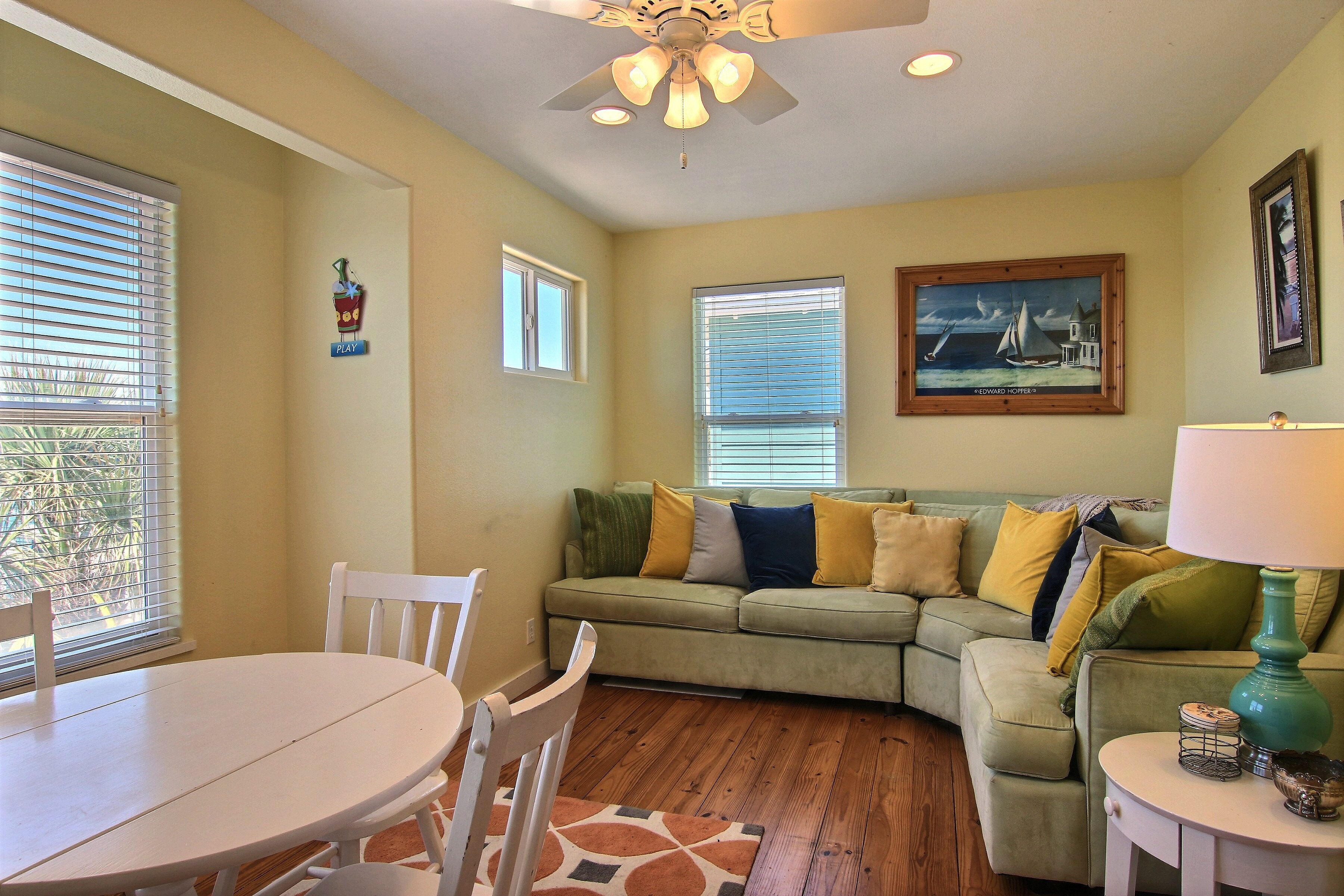 A living room with a green sofa, a white dining table, and a ceiling fan.
